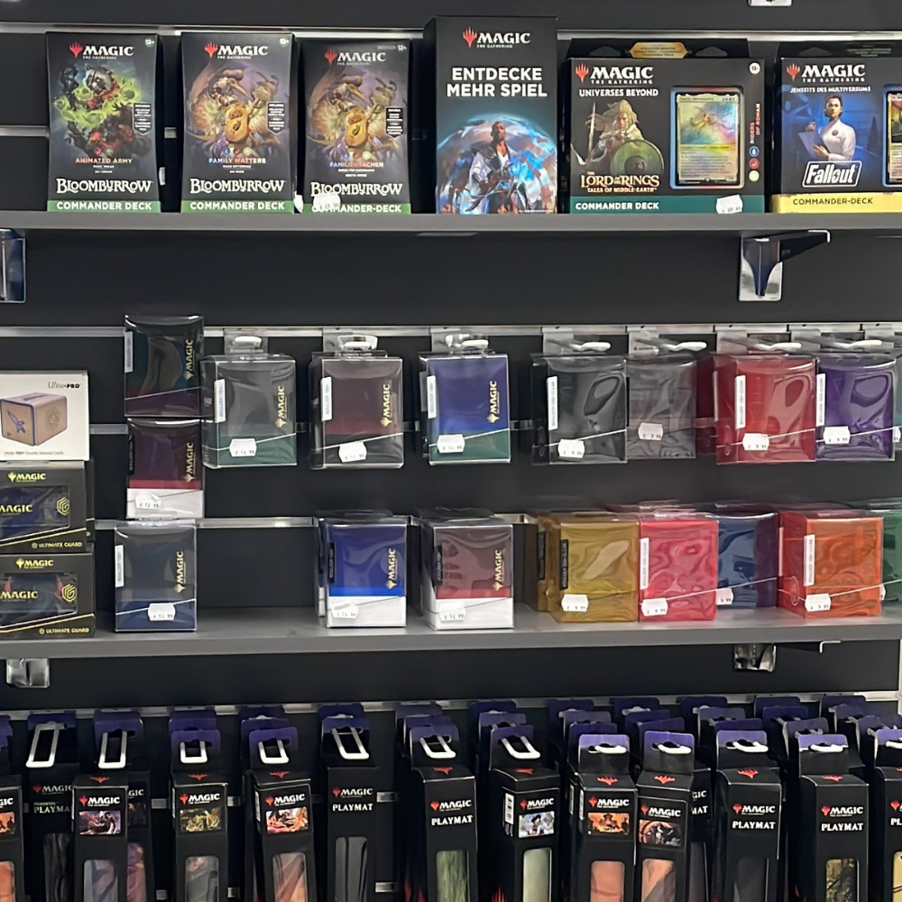 Regal im Trinket-Mage-Shop mit Magic-The-Gathering-Commander-Decks, Deckboxen, Kartenhüllen und Spielmatten.