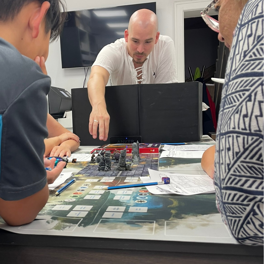 Mehrere Personen spielen gemeinsam ein Tabletop-Spiel an einem Spieltisch unter Anleitung einer weiteren Person.