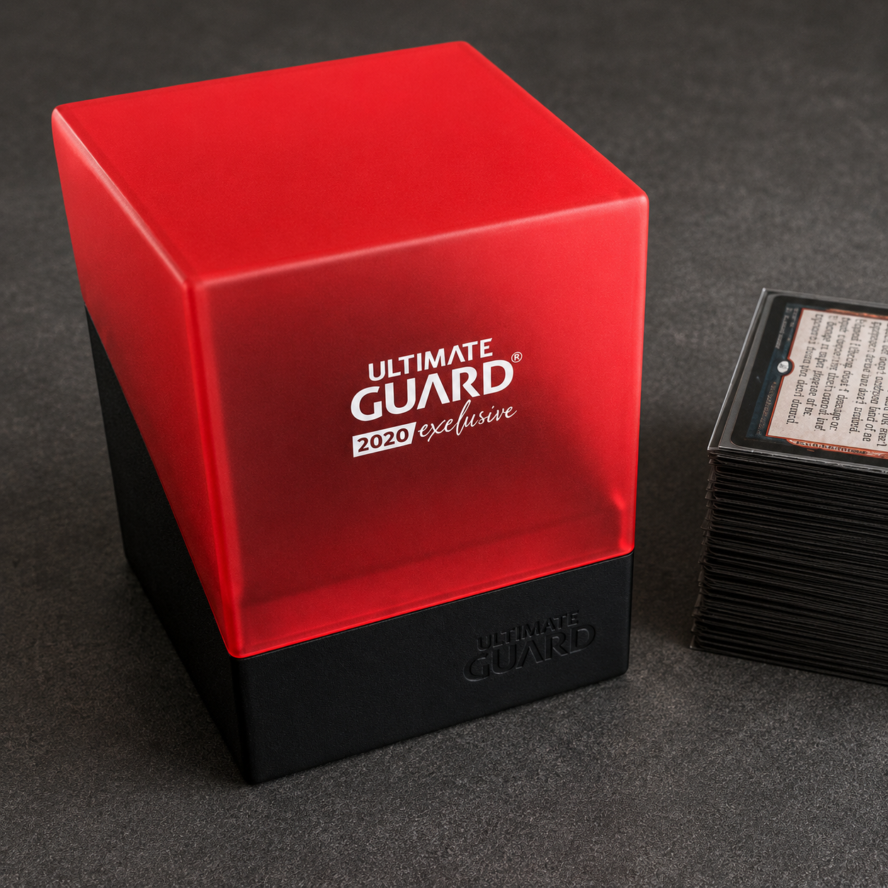 Rote und schwarze Ultimate Guard Deckbox neben einem Stapel Sammelkarten auf dunklem Hintergrund.