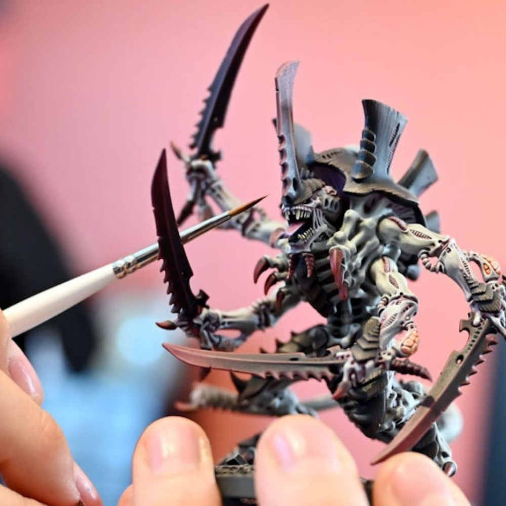 Eine Tyraniden-Miniatur aus Warhammer 40.000 wird mit einem feinen Pinsel bemalt.