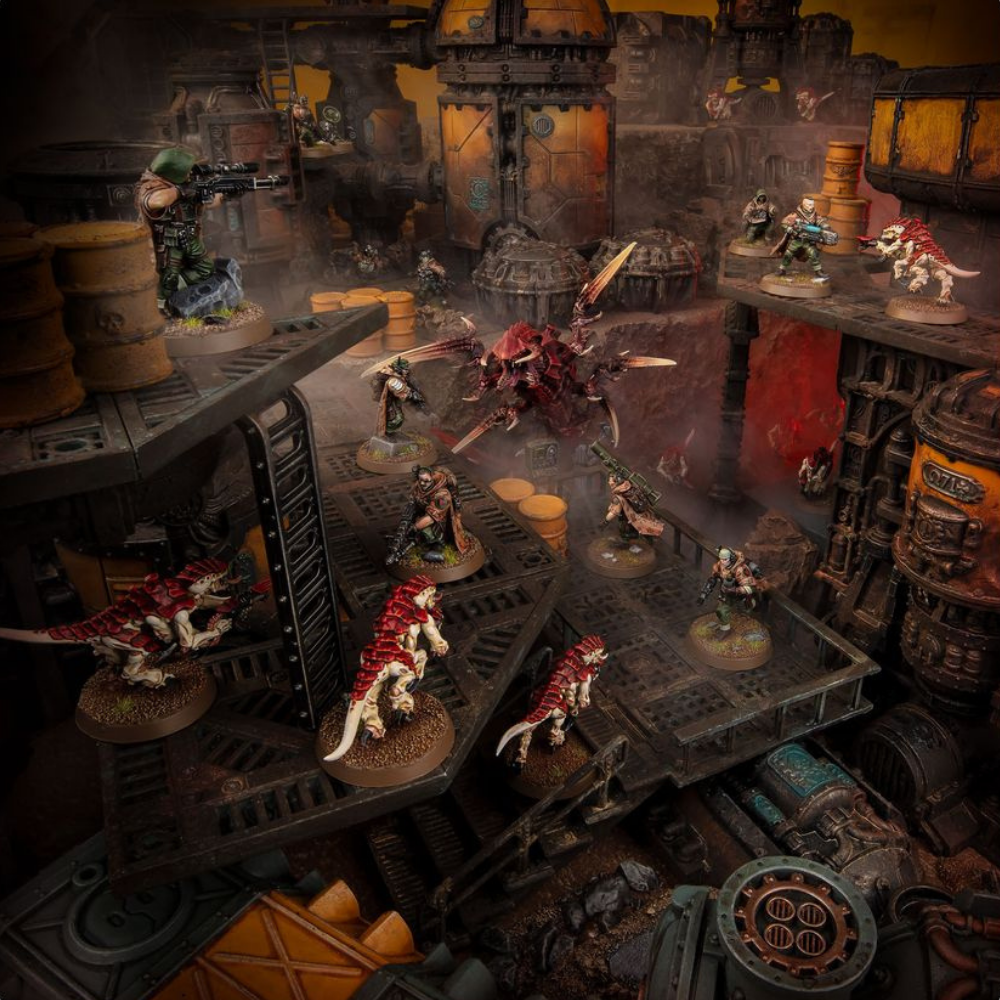Warhammer-40.000-Miniaturen kämpfen auf einem mehrstöckigen industriellen Spielfeld mit Plattformen und Rohren.