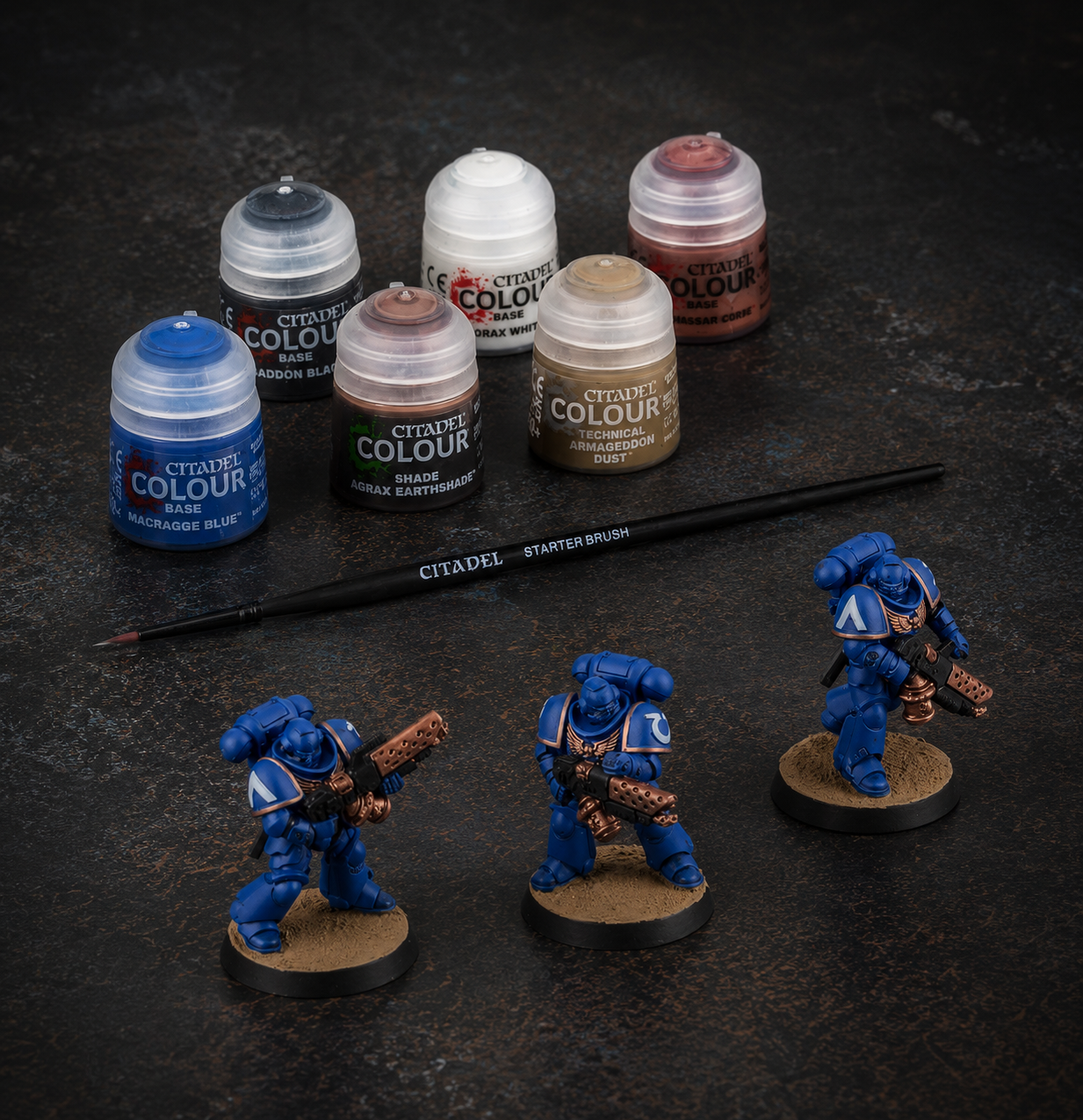 Drei blaue Warhammer-40.000-Ultramarines-Miniaturen stehen vor Citadel-Farben und einem Starterpinsel.